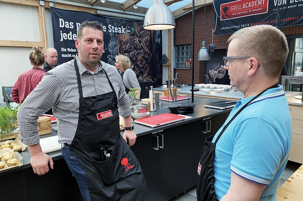 Kochevent Mann mit Schürze lehnt sich an Kochinsel